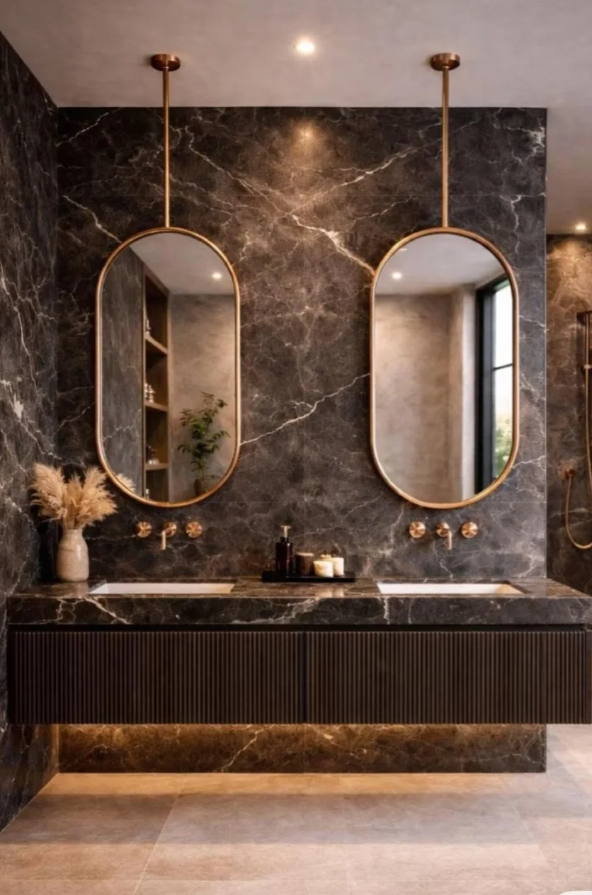 Bathroom with dark marble walls, a floating fluted vanity and two brass-framed oval mirrors